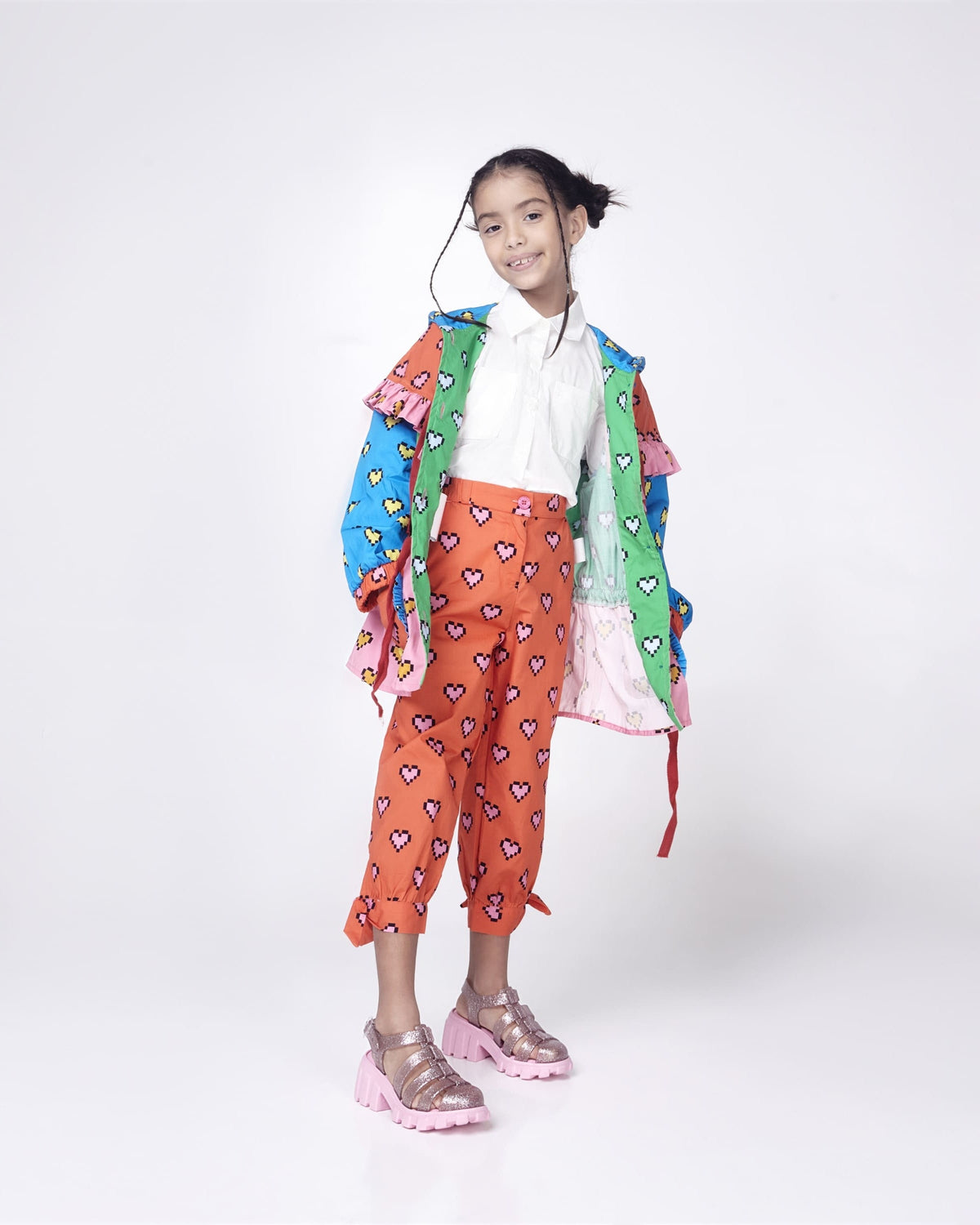 Child model in a white shirt, blue jacket and orange patterned pants wearing a pair of glitter pink Megan kids heel sandals.