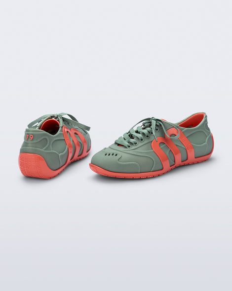 Back and side view of a pair of green Motion sneakers with orange colored sole and M monogram on side and 79 on heel