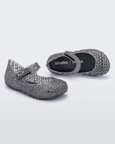 An angled top and side view of a pair of black glitter Mini Melissa Campana flats with a snap strap for baby and an open woven texture.