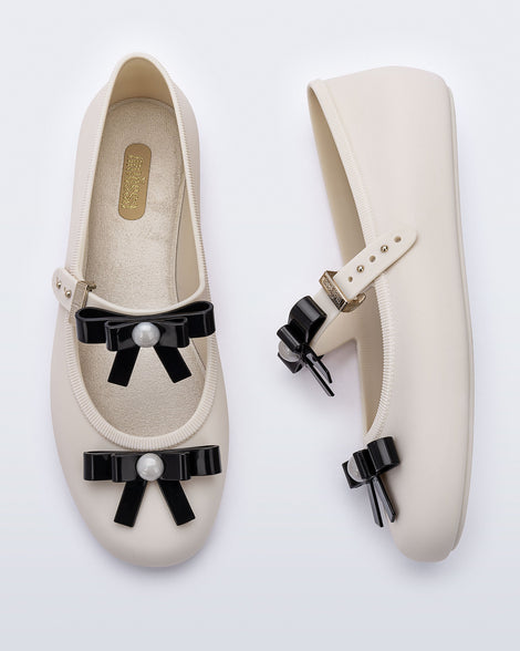 Top and side view of a pair of beige Soft Ballerina Bow flats with black bows and a pearl in the center of each bow
