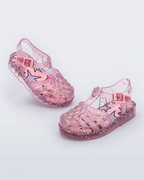 Angled view of a pair of clear pink Possession baby sandals with star glitter