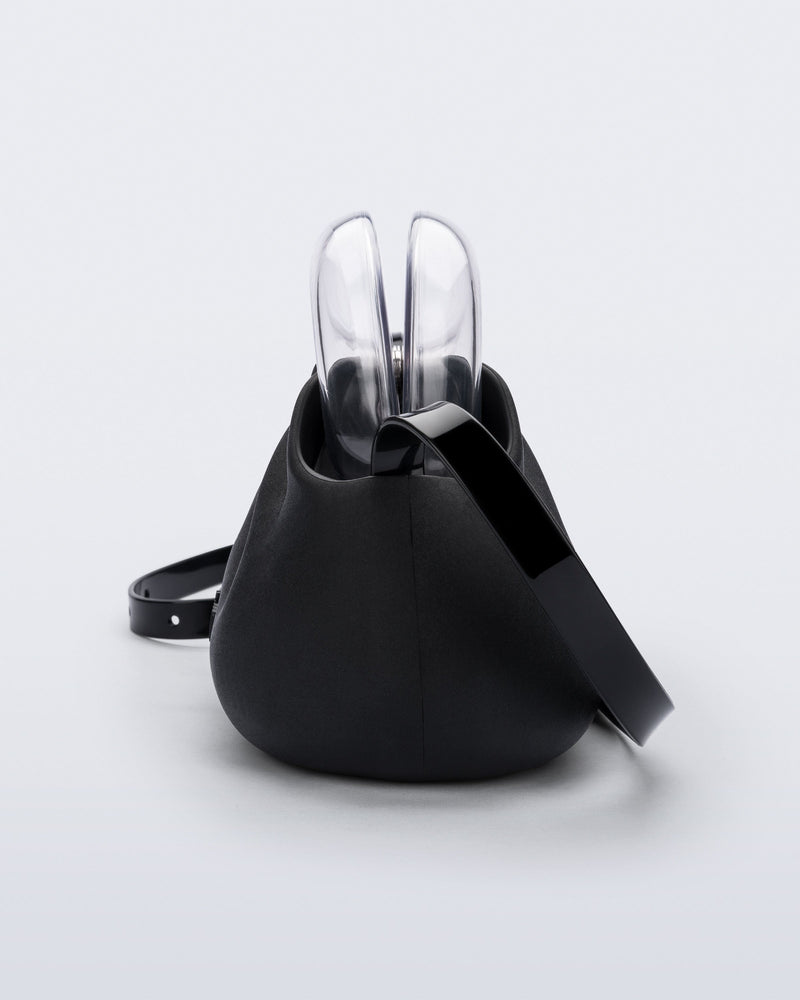 Side view of a small black bag with clear clutch and long strap