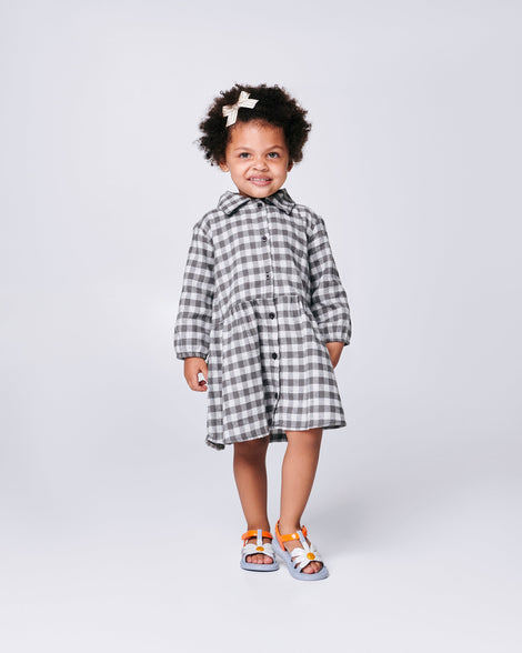 Child model in a black and white dress wearing a pair of blue baby Hip Bloomy sandal with orange strap and white flower