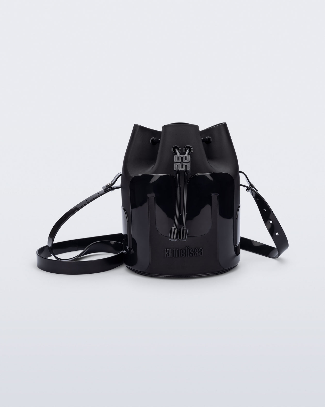 Side view of a Melissa Station bucket bag in Black. The bag has an adjustable shoulder strap and a drawstring top closure. The Melissa logo is on the bottom center of the front of the bag. 