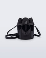 Side view of a Melissa Station bucket bag in Black. The bag has an adjustable shoulder strap and a drawstring top closure. The Melissa logo is on the bottom center of the front of the bag. 