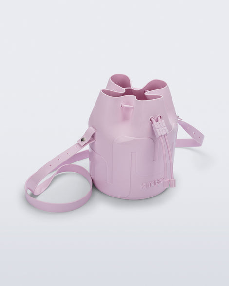 Angled view of a Melissa Station bucket bag in Light Pink. The bag has an adjustable shoulder strap and a drawstring top closure. 