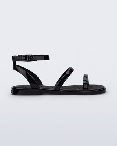 Side view of the Melissa Heat Sandal. This is a flat sandal with a multiple straps, one across the toes, mid part of the foot, and a buckle strap around the ankle with a supporting strap that connects the ankle strap to the sole of the shoe. The straps, insole, outsole, and buckles on the ankle strap are black. The insole is embossed with a geometric pattern. 