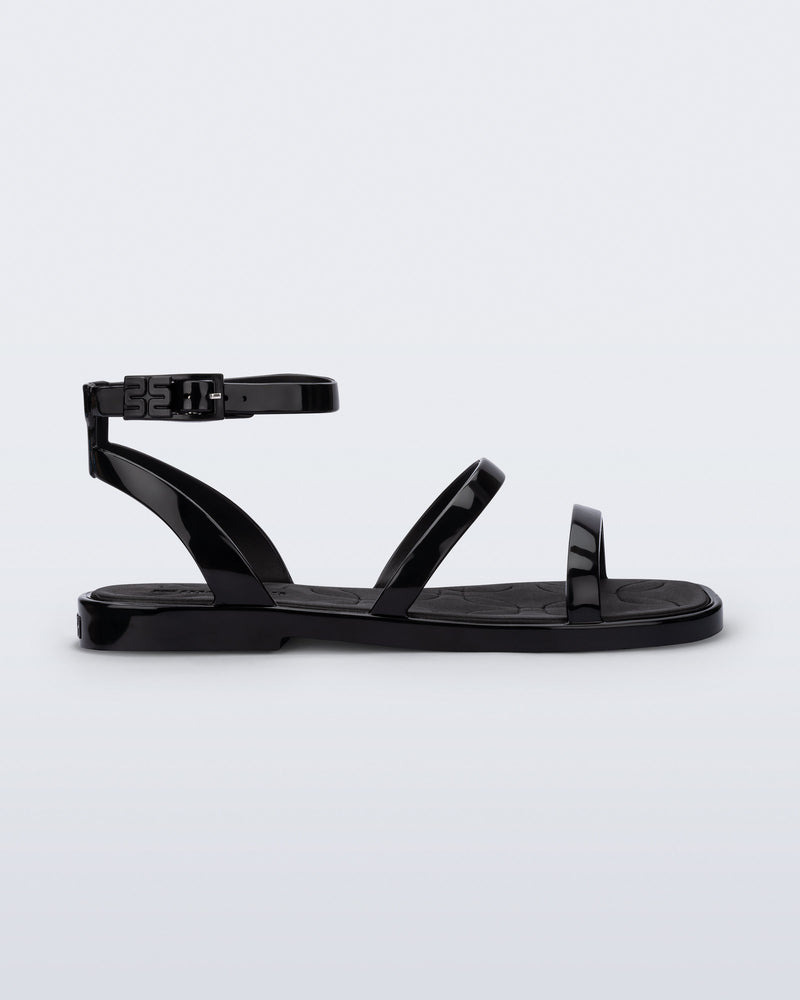 Side view of the Melissa Heat Sandal. This is a flat sandal with a multiple straps, one across the toes, mid part of the foot, and a buckle strap around the ankle with a supporting strap that connects the ankle strap to the sole of the shoe. The straps, insole, outsole, and buckles on the ankle strap are black. The insole is embossed with a geometric pattern. 