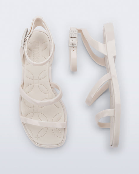 Top and side view of a pair of Melissa Heat Sandals. This is a flat sandal with a multiple straps, one across the toes, mid part of the foot, and a buckle strap around the ankle with a supporting strap that connects the ankle strap to the sole of the shoe.  The straps, insole, outsole, and buckles on the ankle strap are beige. The insole is embossed with a geometric pattern. 