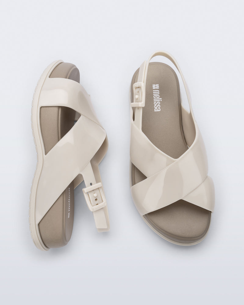 Top and side view of a pair of Melissa Mare platform sandals. This sandal has two cross straps across the front part of the foot with a thin buckle strap attached. The straps and outsole are beige while the platform insole is a darker beige. 