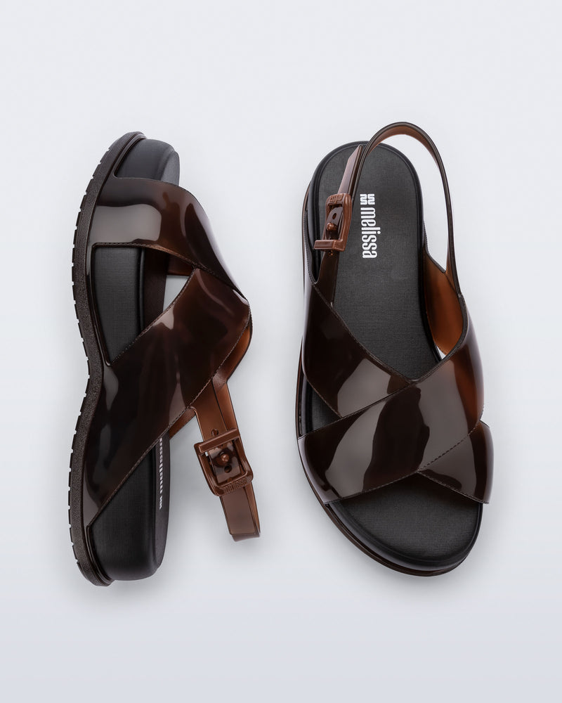Top and side view of a pair of Melissa Mare platform sandals. This sandal has two cross straps across the front part of the foot with a thin buckle strap attached. The straps and outsole are brown while the platform insole is black. 