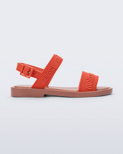 Side view of the Melissa Mar Sandal with Melissa logo embossed into the straps. There are two embossed straps that go across the foot; 1 across the toes and the other across the main part of the foot. The main foot strap has an ankle strap attached with a buckle closure. The straps and buckle are orange and the sole of the shoe is brown. The buckle placement is on the outside of the ankle strap. 