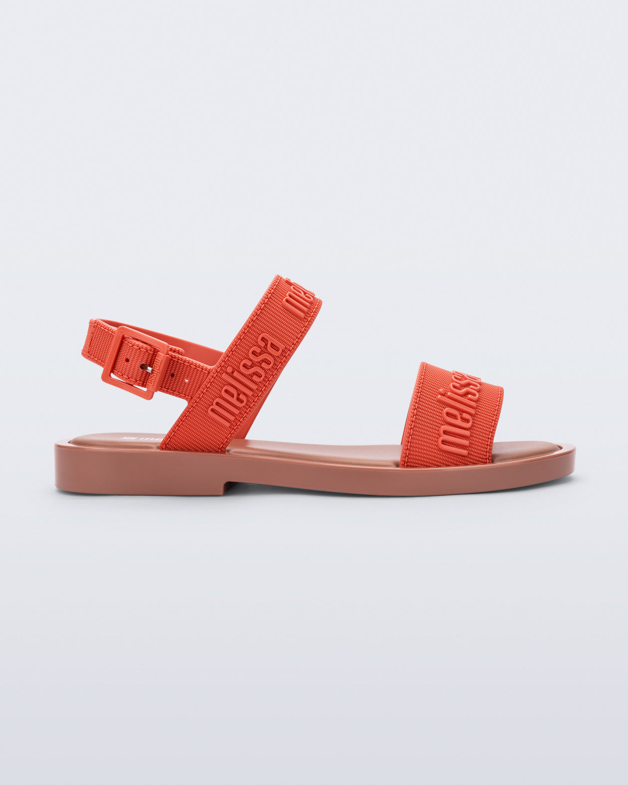 Side view of the Melissa Mar Sandal with Melissa logo embossed into the straps. There are two embossed straps that go across the foot; 1 across the toes and the other across the main part of the foot. The main foot strap has an ankle strap attached with a buckle closure. The straps and buckle are orange and the sole of the shoe is brown. The buckle placement is on the outside of the ankle strap. 