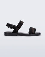 Side view of the Melissa Mar Sandal with Melissa logo embossed into the straps. There are two embossed straps that go across the foot; 1 across the toes and the other across the main part of the foot. The main foot strap has an ankle strap attached with a buckle closure. The straps ,buckle and sole of the shoe is black. The Melissa logo on the straps has a black metallic finish. . The buckle placement is on the outside of the ankle strap. 