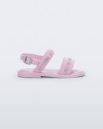 Side view of the Mini Melissa Mar Sandal with Mini Melissa logo embossed into the straps. There are two embossed straps that go across the foot; 1 across the toes and the other across the main part of the foot. The main foot strap has an ankle strap attached with a buckle closure. The straps ,buckle and sole of the shoe is pink. The Melissa logo on the straps has a silver metallic finish. . The buckle placement is on the outside of the ankle strap. 