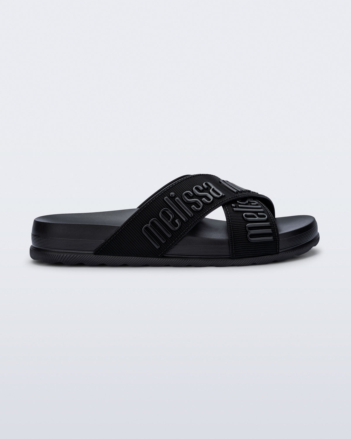 Side view of the Melissa Cozy slide sandals. The slide has two cross straps with Melissa logo embossed onto the straps. The color of the shoe is black. 