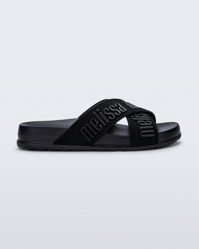 Side view of the Melissa Cozy slide sandals. The slide has two cross straps with Melissa logo embossed onto the straps. The color of the shoe is black. 