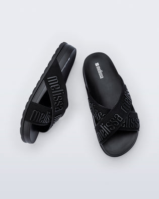 Top and side view of a pair of Melissa Cozy slide sandals. The slide has two cross straps with Melissa logo embossed onto the straps. The color of the shoe is black.