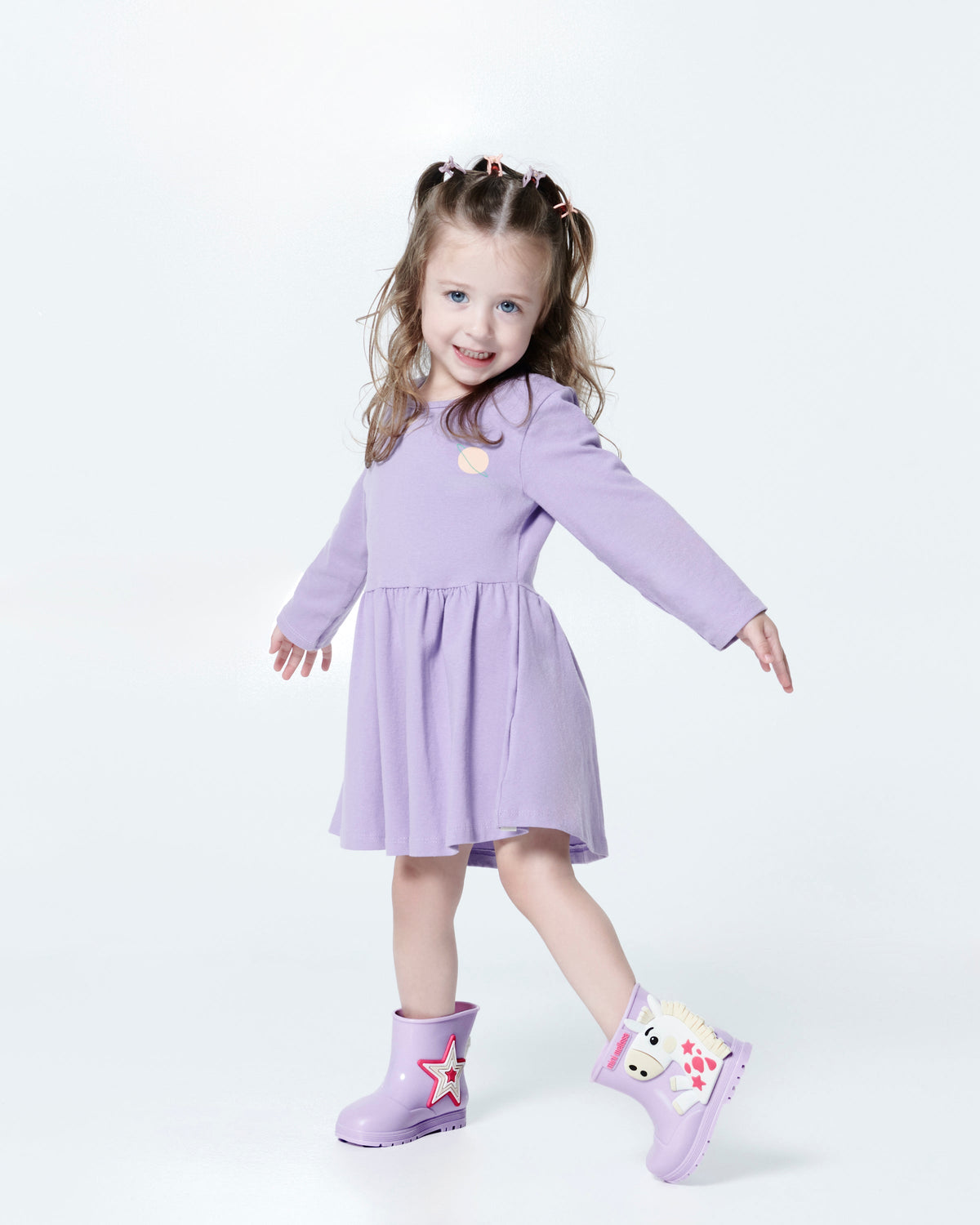 Child model in a lilac dress wearing a pair of lilac Welly Wonderland baby boots with white pony on one shoe and star on the other