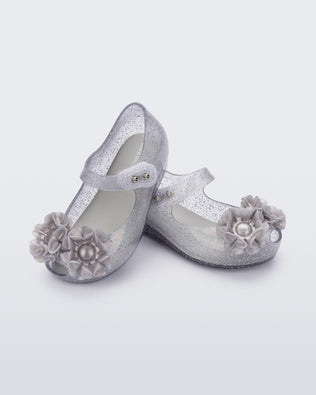 Angled view of a pair of clear grey glitter Ultragirl Springtime baby flat with grey flower and peep toe.