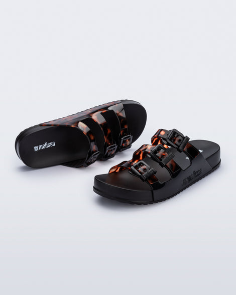Top and angled view of a pair of black Cozy Stripes slides with tortoise colored straps