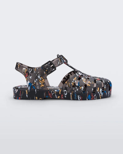 Side view of a Mini Melissa Possession fisherman sandal in black with all over Disney character print. There is a buckle closure on the side of the ankle strap. 