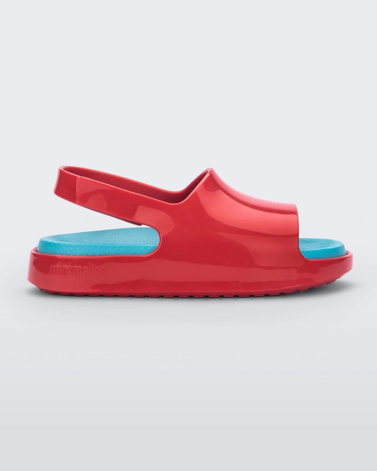 Side view of a red Mini Melissa Cloud sandals with a blue insole, red base and back velcro strap.