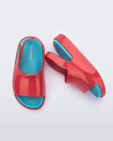 A top and side view of a pair of red Mini Melissa Cloud sandals with a blue insole, red base and back velcro strap.