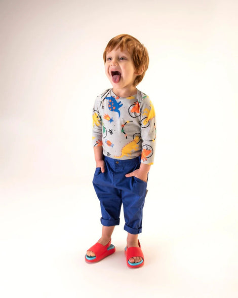 A model posing for a picture wearing a pair of red Mini Melissa Cloud sandals with a blue insole, red base and back velcro strap.