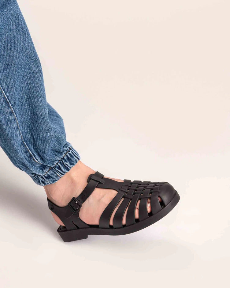 Model's leg wearing a Melissa Possession fisherman sandal in black with a matte finish, cut out fishermen strap detail and buckle closure