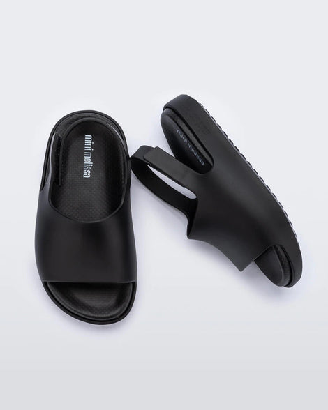 A top and side view of a pair of matte black Mini Melissa Cloud sandals with a black insole, base and back velcro strap.