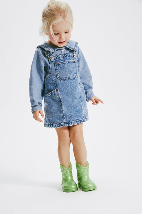 Child model in a jean overall dress wearing a pair of pearly green Texas baby boots
