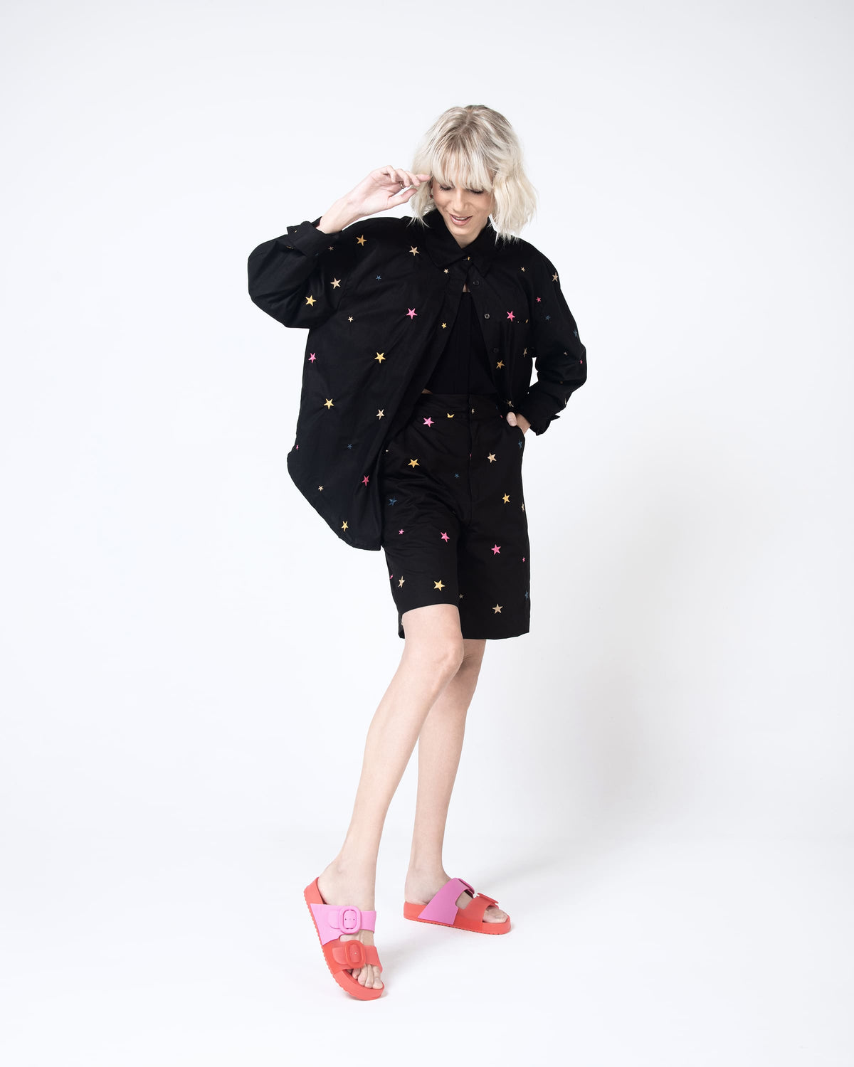 A model posing for a picture wearing a black patterned top and bottoms and a pair of Red/Pink Melissa Cozy slides with two red and pink straps with a buckle detail.