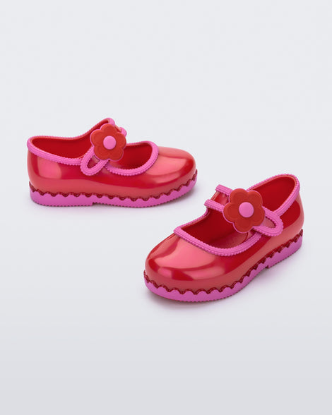 Side and angled view of a pair of red with pink trim Hip Ballerina baby flats with strap with flower
