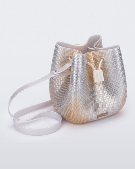 Angled view of a silver/gold Lux bucket bag with drawstring and strap