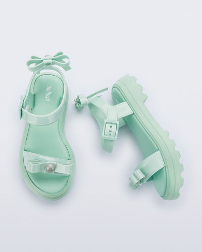 Side and top view of a pair of green Town Bow sandals with bows and a pearl in the center of each bow