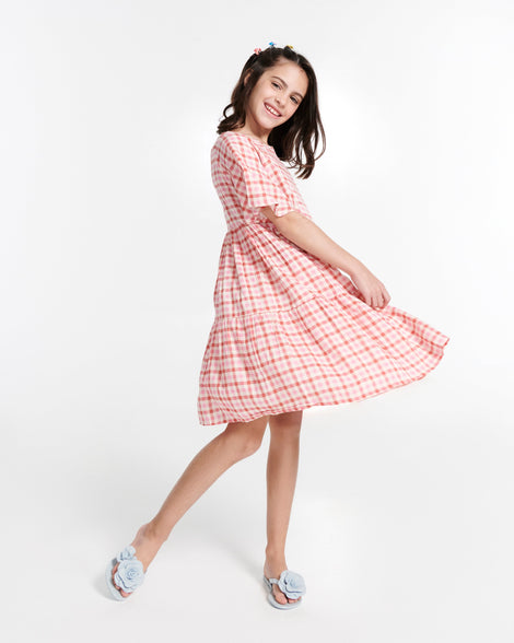 Child model in a gingham dress wearing a pair of blue Harmonic Petals kids flip flops with flowers