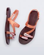 Top and side view of a pair of orange Iris sandals with burgundy sole and rose gold upper embellishments