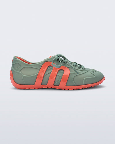 Side view of a green Motion sneaker with orange colored sole and M monogram