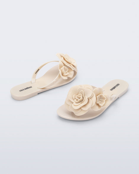 Back and angled view of a pair of beige Harmonic Petals kids flip flops with flowers