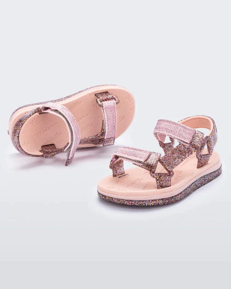 Angled view of a pair of pink and glitter Mini Melissa Papete sandals.
