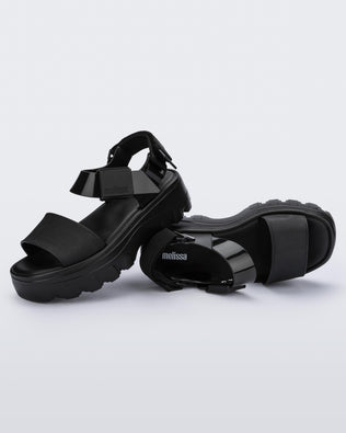 An angled top and side view of a pair of black platform Melissa Kick Off sandals with two straps.