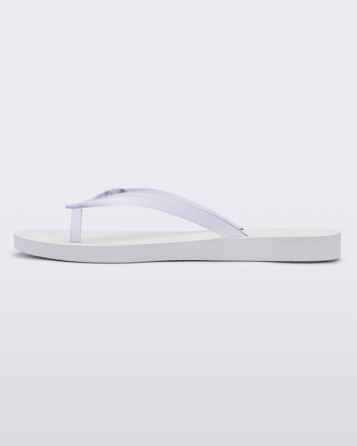 An inner side view of a white/clear Melissa Sun Venice flip flop with a white sole and clear straps with "melissa" on one strap.