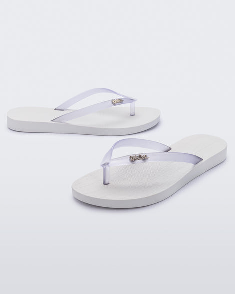 An angled front and side view of a pair of white/clear Melissa Sun Venice flip flops with a white sole and clear straps with 