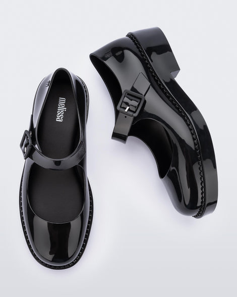 A top and side view of a pair of black Melissa Lola loafers with a rounded toe and a black strap and buckle.