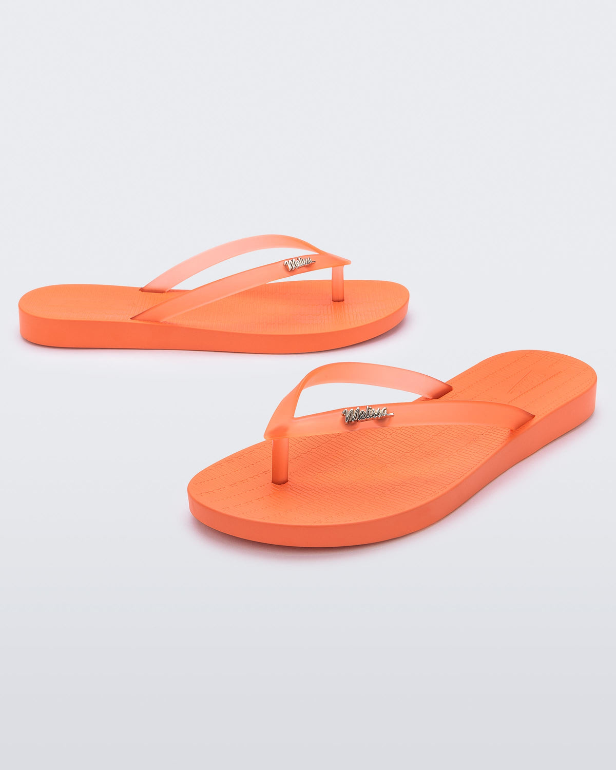 An angled front and side view of a pair of orange Melissa Sun Venice flip flops with "melissa" on the strap.
