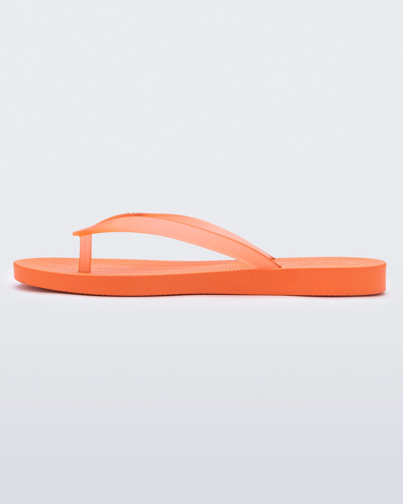 An inner side view of an orange Melissa Sun Venice flip flop with "melissa" on the strap.