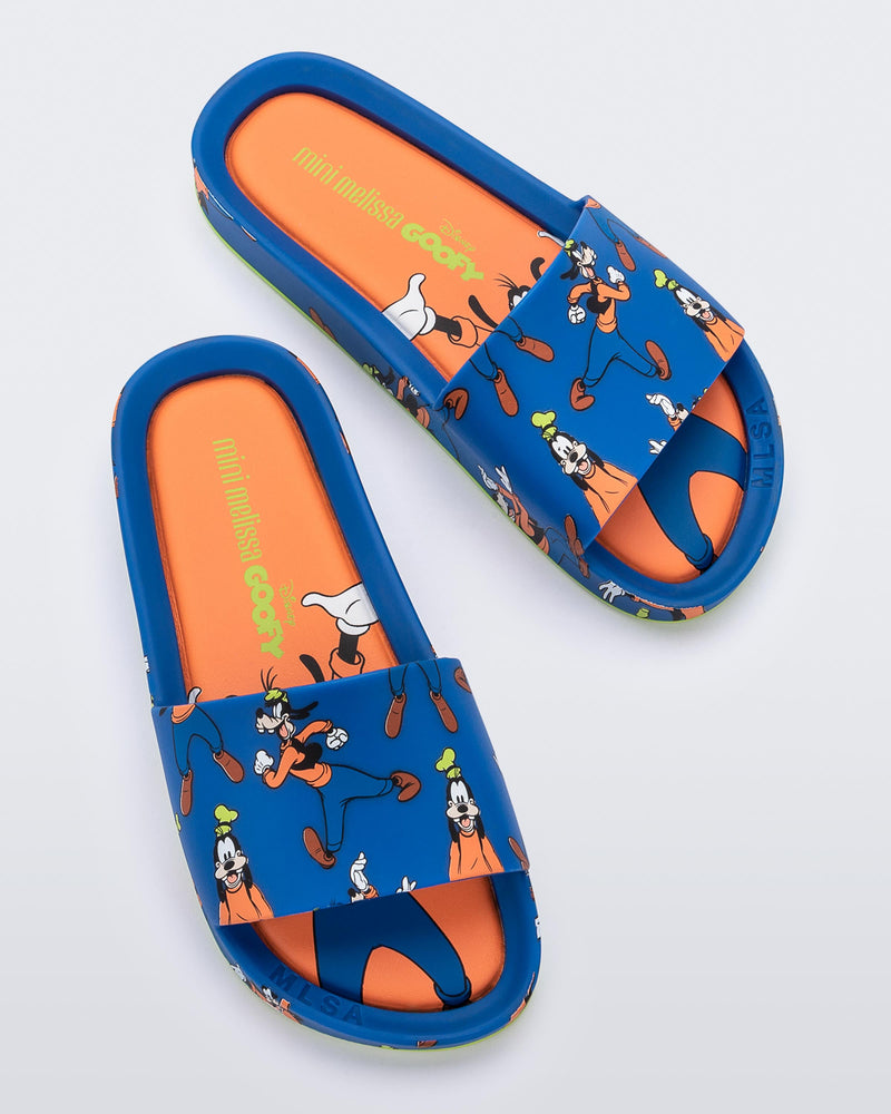 Top view of a pair of blue Mini Melissa Beach slides with a blue base and a pattern of Disney's Goofy in different poses.