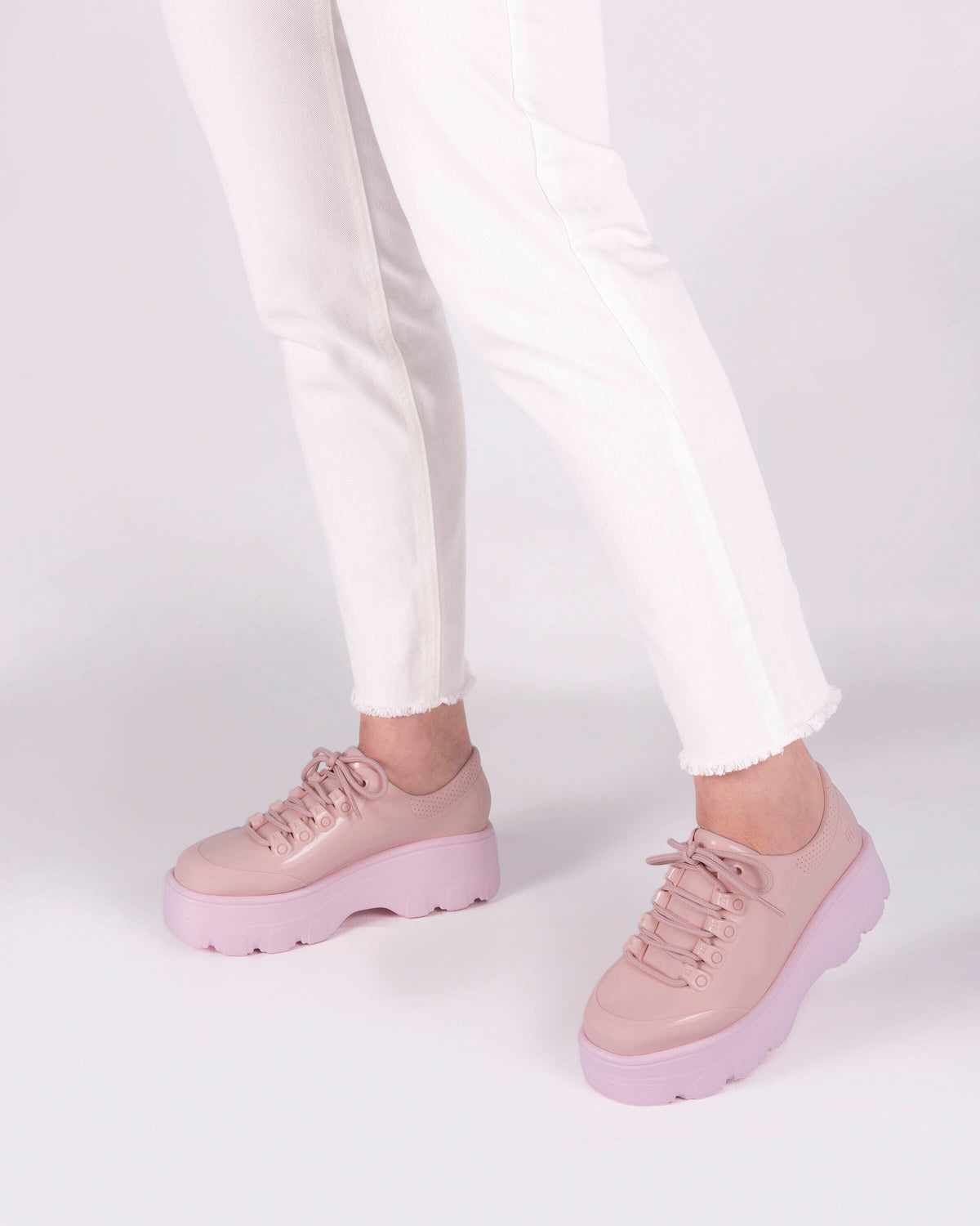 A model's legs wearing white jeans and a pair of pink platform Melissa Kick Off Sneaker with laces.