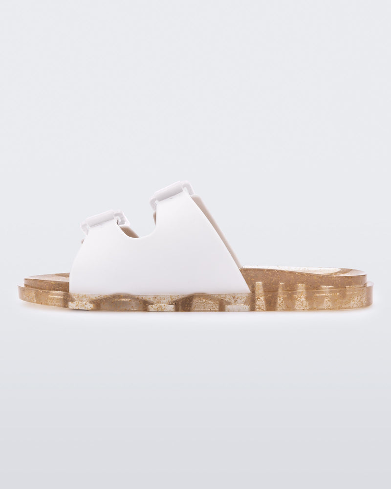 An inner side view of a Beige Mini Melissa Wide Slide with a white top with two white buckles and a beige sole.